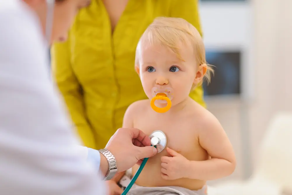 Médico auscultando con estetoscopio el pecho de un bebé en brazos de su mamá