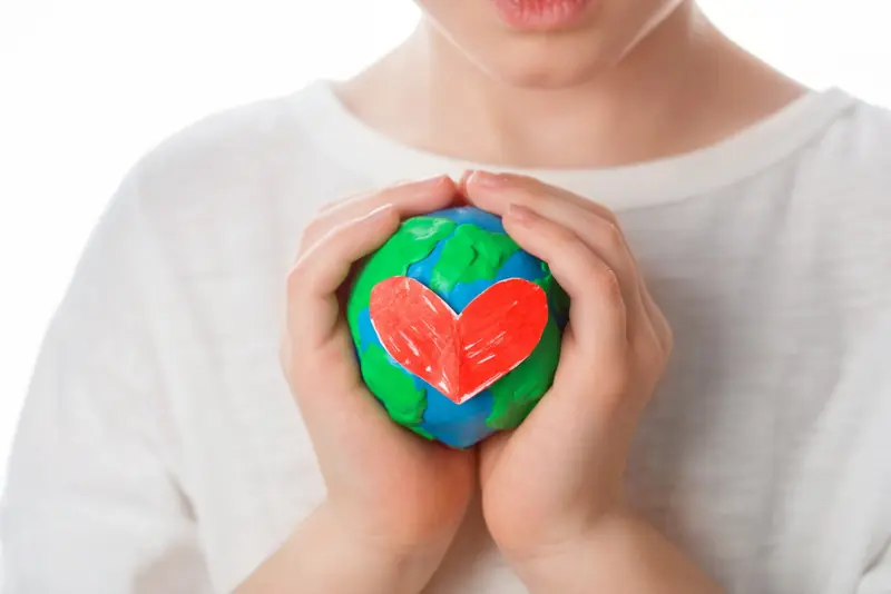 Manos de un niño sosteniendo un globo terráqueo de plastilina con un corazón rojo