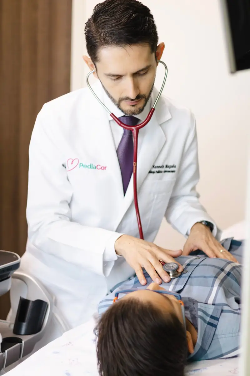 Dr. Kenneth Magaña de PediaCor auscultando con estetoscopio a un paciente en cama hospitalaria