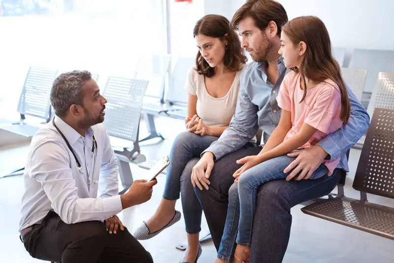 Médico conversando con una madre y sus hijas en una sala de espera